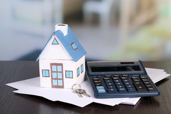 A miniature of a home beside a set of keys and calculator on top of a stack of documents